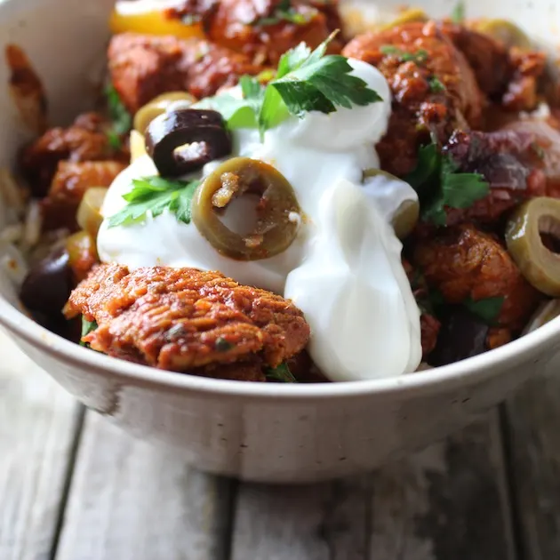 Close up bowl of chicken with Moroccan seasonings, topped with yogurt