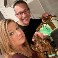 2 people holding live lobsters over pot