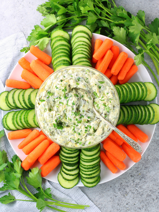 glass bowl of spinach artichoke dip on a platter with fresh veggies