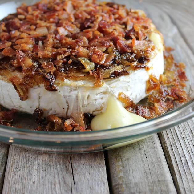 Eye level close up partial baked brie topped with bacon and caramelized onions in a pie dish