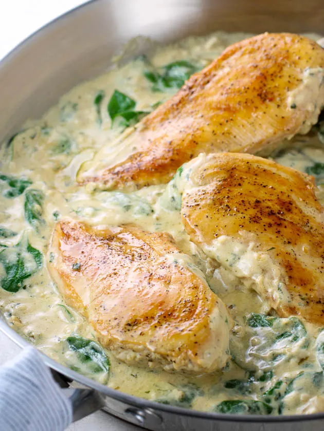 eye level close up chicken breasts in a pan of creamy sauce with spinach